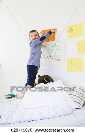 Stock Image - Boy hanging drawing on bedroom wall. Fotosearch