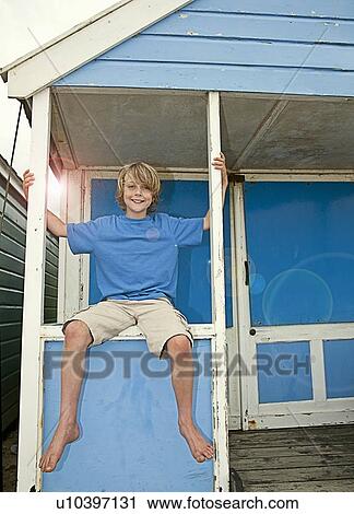 Stock Image - Boy sitting in windowsill of hut. Fotosearch