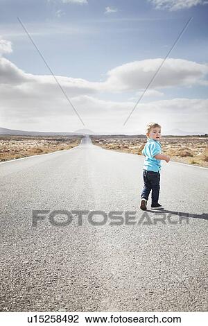 Stock Image - Boy walking on paved rural road. Fotosearch