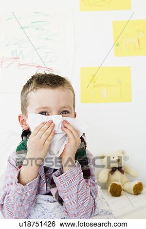 Stock Photograph - Boy wiping his nose in bed. Fotosearch