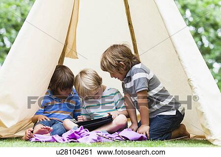 Stock Image - Boys using tablet computer in tent. Fotosearch