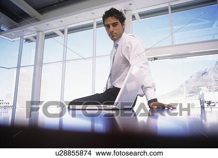 Businessman sitting on desk in office View Large Photo Image Picture - Businessman sitting on desk in office. Fotosearch