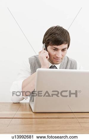 Businessman using laptop and cell phone View Large Photo Image Stock Image - Businessman using laptop and cell phone. Fotosearch