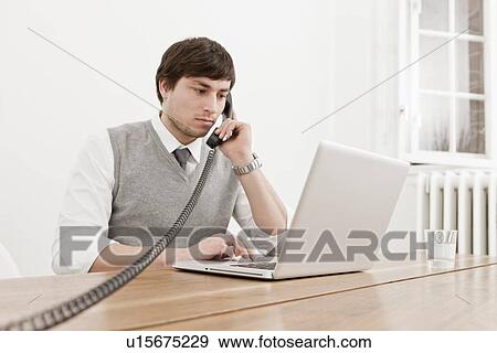 Stock Photo - Businessman using laptop and telephone. Fotosearch