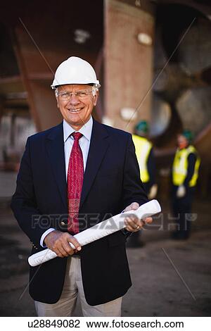 Stock Image - Businessman with blueprints on dry dock. Fotosearch