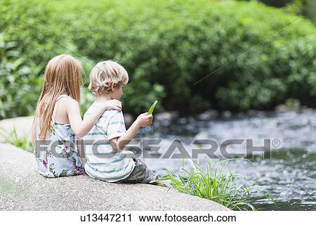 Stock Image - Children sitting on rock together. Fotosearch