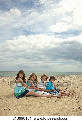 Stock Image - Children sitting together on beach. Fotosearch
