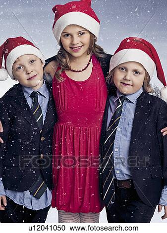 Stock Image - Children wearing Santa hats in snow. Fotosearch