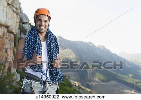 Stock Image - Climber holding coiled rope on mountain. Fotosearch