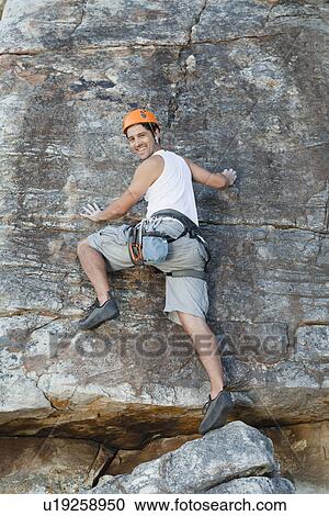 Stock Image - Climber scaling steep rock face. Fotosearch