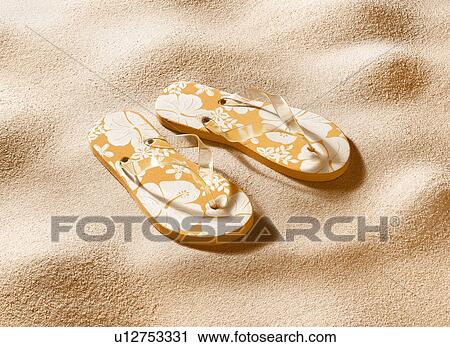 Stock Image - Close up of flip flops in sand. Fotosearch