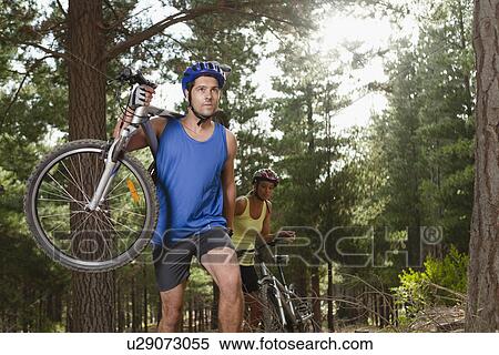 Stock Photography - Couple carrying mountain bikes in forest. Fotosearch