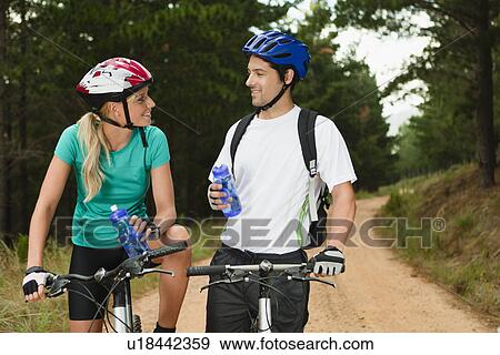 Stock Photo - Couple drinking water on mountain bikes. Fotosearch