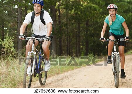 Couple mountain biking on dirt road View Large Photo Image Stock Photo - Couple mountain biking on dirt road. Fotosearch
