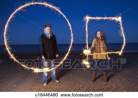 Stock Image - Couple playing with sparklers on beach. Fotosearch