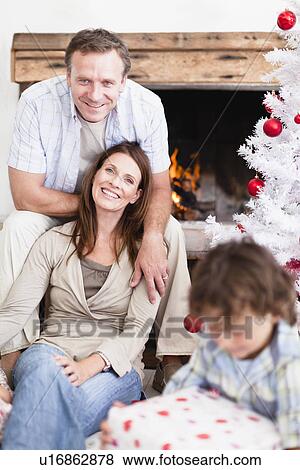 Stock Photo - Couple relaxing by Christmas tree. Fotosearch