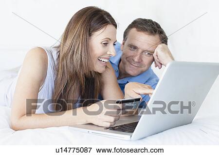 Couple shopping online on bed View Large Photo Image Stock Photo - Couple shopping online on bed. Fotosearch