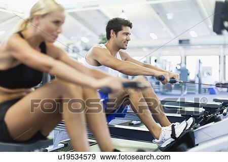 Stock Photo - Couple using rowing machines in gym. Fotosearch