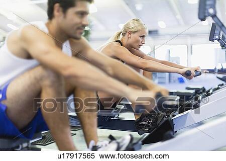 Stock Photography - Couple using rowing machines in gym. Fotosearch