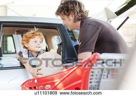 Stock Photo - Father and son loading groceries in car. Fotosearch