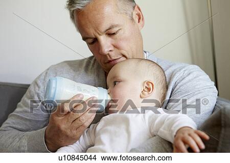 Picture - Father bottle feeding baby on sofa. Fotosearch