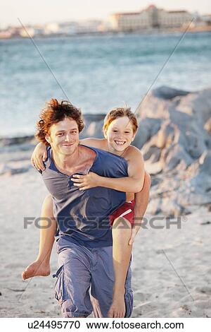 Father carrying son piggyback on beach View Large Photo Image Stock Image - Father carrying son piggyback on beach. Fotosearch