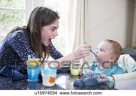 Girl feeding baby brother at table View Large Photo Image Picture - Girl feeding baby brother at table. Fotosearch