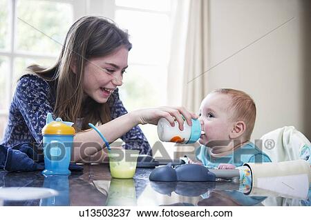 Stock Photo - Girl feeding baby brother at table. Fotosearch