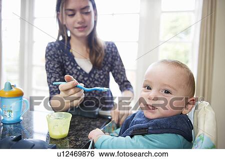 Stock Photograph - Girl feeding baby brother at table. Fotosearch