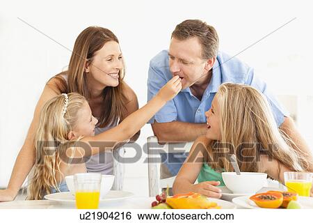Stock Photograph - Girl feeding father at breakfast table. Fotosearch