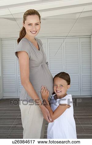 Stock Photo - Girl hugging pregnant mothers belly. Fotosearch