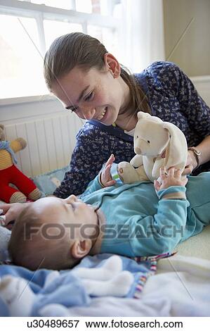 Stock Photo - Girl playing with baby brother on bed. Fotosearch