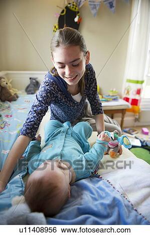 Stock Photograph - Girl playing with baby brother on bed. Fotosearch