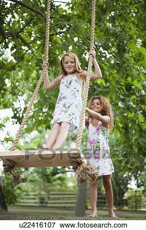 Girl pushing friend on tree swing View Large Photo Image Stock Photo - Girl pushing friend on tree swing. Fotosearch