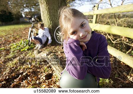 Stock Photo - Girl sitting on log in meadow. Fotosearch