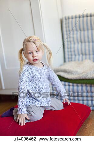 Stock Image - Girl sitting on pillow in living room. Fotosearch