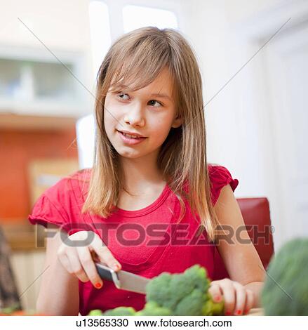 Stock Image - Girl slicing vegetables in kitchen. Fotosearch
