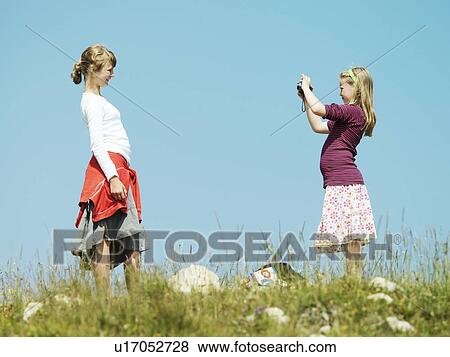Stock Photo - Girl taking picture of friend outdoors. Fotosearch