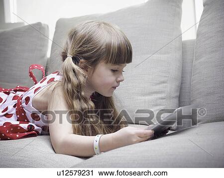 Stock Image - Girl using tablet computer on sofa. Fotosearch