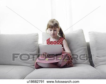 Stock Image - Girl using tablet computer on sofa. Fotosearch
