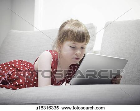 Stock Photography - Girl using tablet computer on sofa. Fotosearch