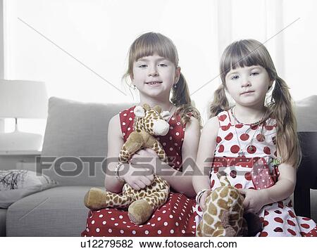 Stock Image - Girls holding stuffed animals on sofa. Fotosearch