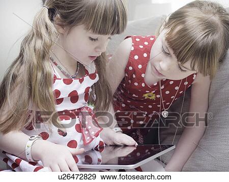 Stock Photo - Girls using tablet computer on sofa. Fotosearch