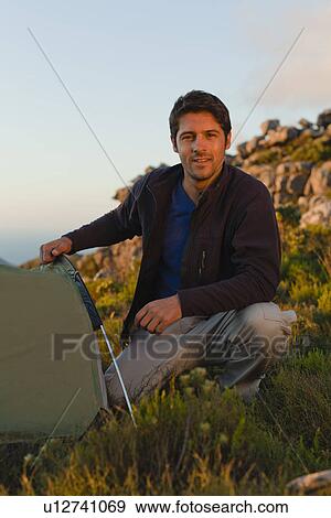 Hiker setting up tent on hillside View Large Photo Image Stock Photo - Hiker setting up tent on hillside. Fotosearch