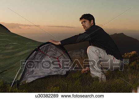 Stock Photo - Hiker setting up tent on hillside. Fotosearch