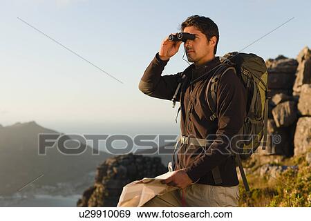 Stock Photo - Hiker using binoculars in rocky field. Fotosearch