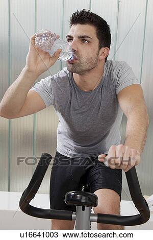 Stock Image - Man drinking water on exercise machine. Fotosearch