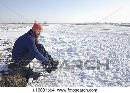 Man lacing up ice skates in snowy field View Large Photo Image Picture - Man lacing up ice skates in snowy field. Fotosearch