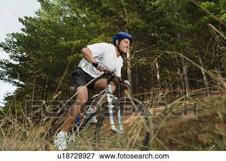 Stock Photo - Man mountain biking on dirt path. Fotosearch