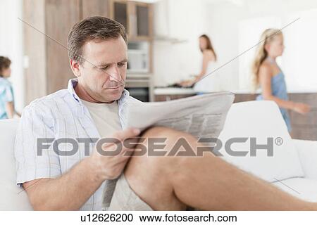 Stock Image - Man reading newspaper on sofa. Fotosearch